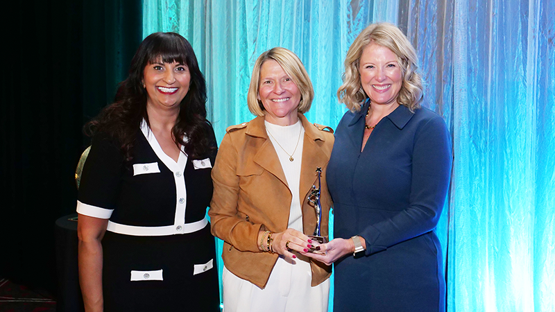 a photo showing three women in professional clothing standing in front of a teal-colored backdrop
